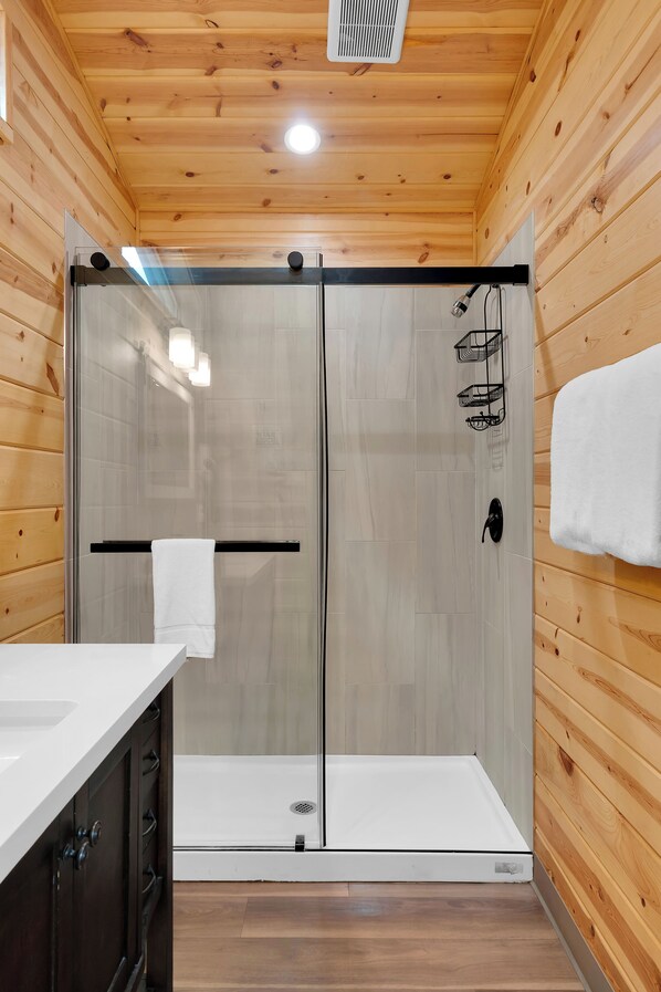 Un baño moderno con paredes de madera, cabina de ducha de vidrio, un lavabo blanco y un perchero para toallas.