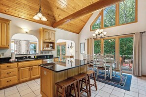 A spacious kitchen with wooden cabinets, a central island, and a dining area with a view of trees. - Spacious Home in Fish Creek | Peloton + Walk to Shops + Close to State Park (Fish Creek)