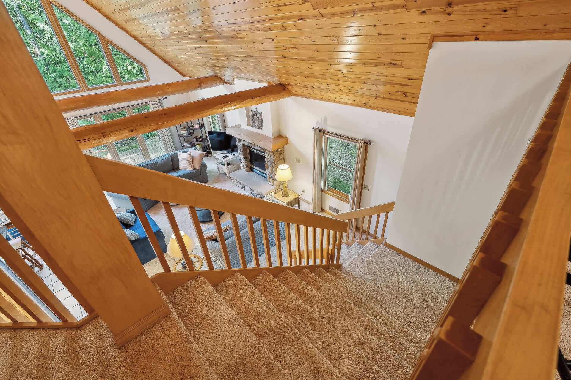 Un escalier en bois mène à un espace de vie comprenant une cheminée, un canapé et un téléviseur.
