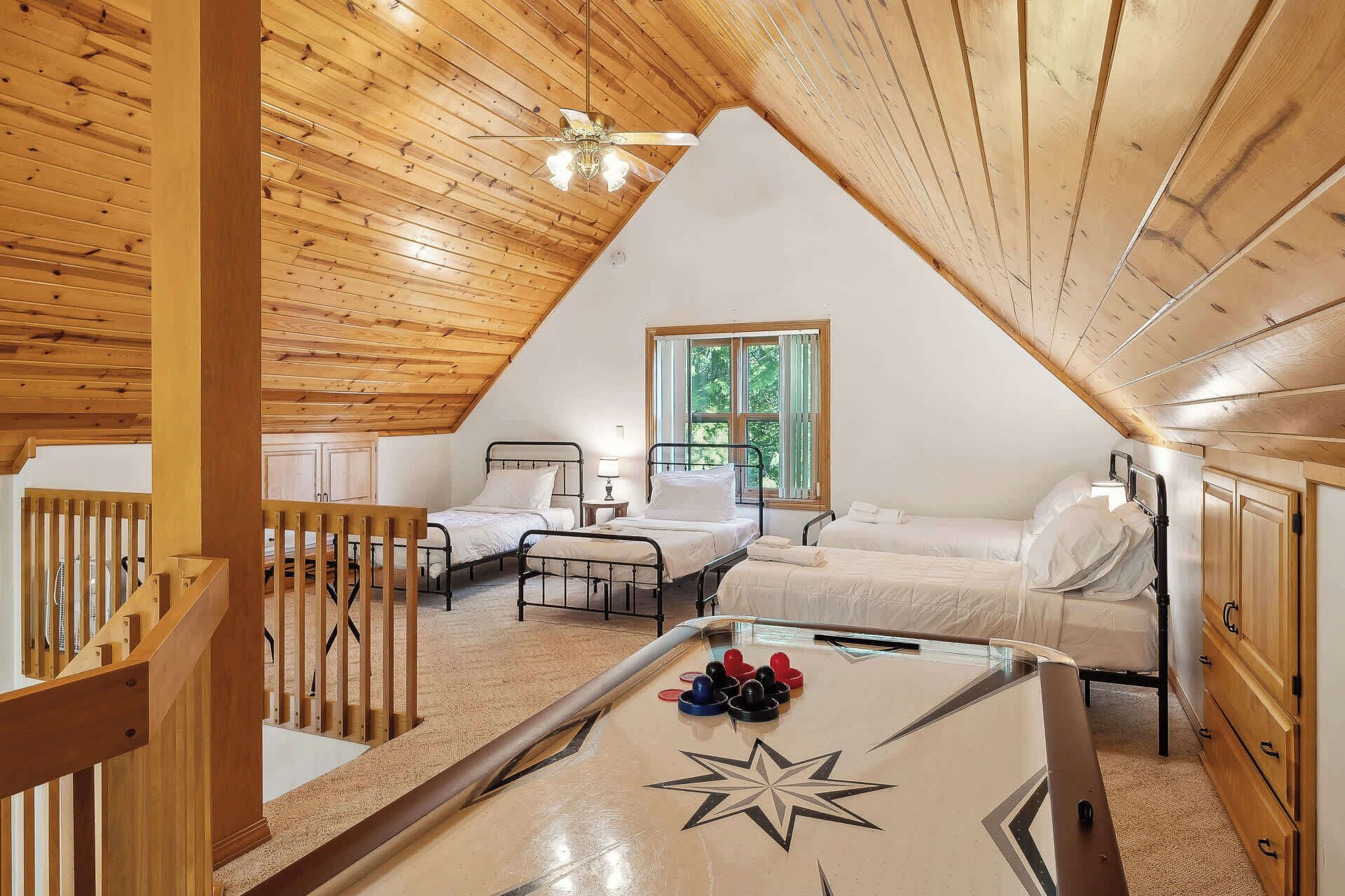Une chambre confortable située dans les combles, avec des poutres en bois, deux lits, un ventilateur de plafond et une table basse ornée d’un motif en forme d’étoiles.