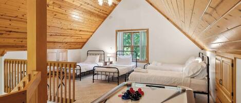 Une chambre confortable située dans les combles, avec des poutres en bois, deux lits, un ventilateur de plafond et une table basse ornée d’un motif en forme d’étoiles.