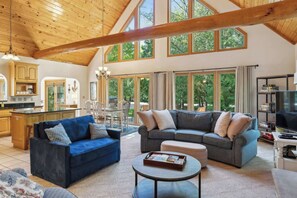 A spacious living room with two sofas, a coffee table, and a dining area with a table and chairs. Large windows provide natural light and views of greenery. - Dog Friendly Home in Fish Creek>Walk to Shopping center + close to State Park (Fish Creek)