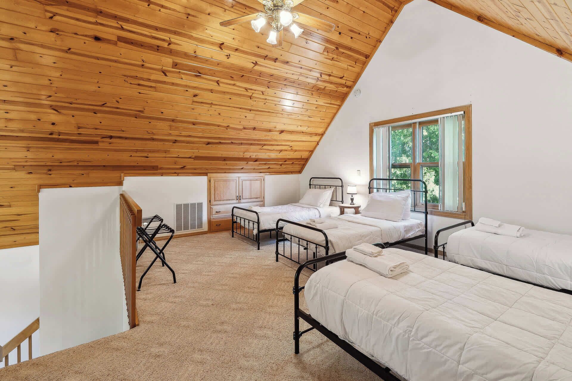 Quarto com duas camas, teto de madeira, janela e radiador.