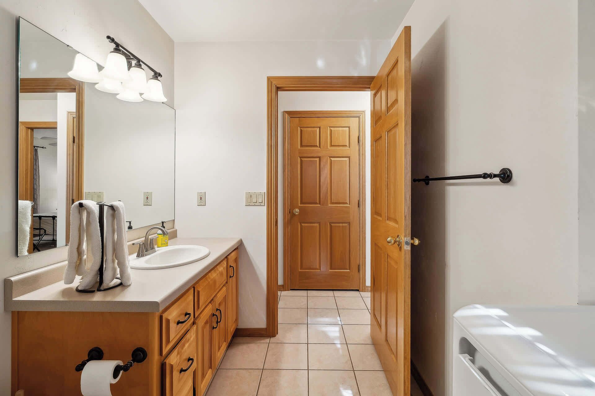 A bathroom with a sink, mirror, towel rack, toilet, and a door leading to another room.
