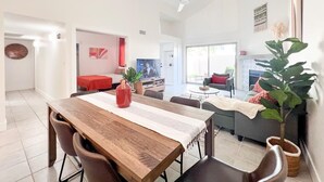 A spacious living area with a wooden dining table, comfortable seating, a large plant, and a television in the background. - Southwestern Serene Oasis located in Chandler, featuring a community pool
 (Chandler)