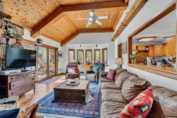 A spacious living room with a large leather sofa, wooden ceiling beams, a stone wall, and a television.