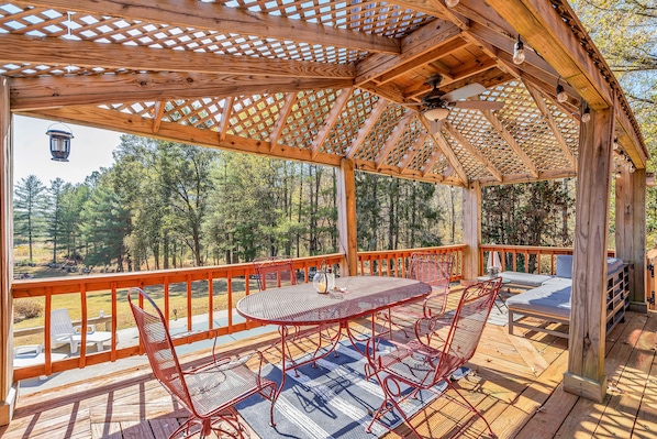 Une terrasse en bois agrémentée d’une pergola, une table ronde avec des chaises et une vue sur la forêt environnante.