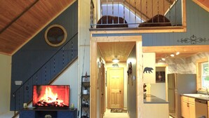 A cozy interior with a fireplace, a staircase, a kitchen, and a dining area. - Cozy Chalet in the Heart of Northern Michigan (Williamsburg)