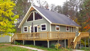 A two-story house with a wooden deck and a staircase leading to a second level. - Cozy Chalet in the Heart of Northern Michigan (Williamsburg)
