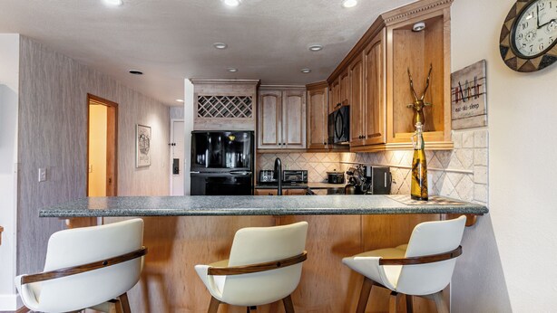 A kitchen with a bar area, wooden cabinets, a refrigerator, a microwave, and a clock on the wall. - Modern home with three balconies, mountain views, and outdoor swimming pool. Walk to hiking trails (Park City)