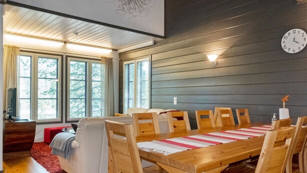 Ein modernes Esszimmer mit einem Holztisch, Stühlen, großen Fenstern und einer Uhr an der Wand.