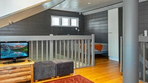 Ein modernes Zimmer mit schrägen Wänden, einem Holzbodenfernseher, einem Fernseher, einem Babybett und einem Fenster.