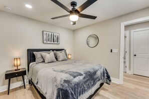 A bedroom with a bed, bedside lamps, a ceiling fan, a wall-mounted mirror, and a door.