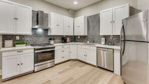 A modern kitchen with white cabinets, stainless steel appliances, and a tiled backsplash. - 4 Bedroom Home Close to Everything (Atlanta)