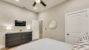 A bedroom with a bed, a dresser, a television, and two doors. - 4 Bedroom Home Close to Everything (Atlanta)