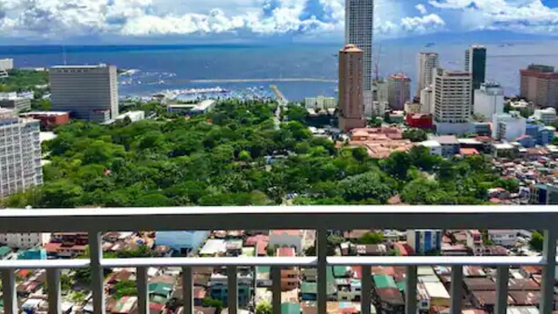 A cityscape with a prominent tall building, dense urban area, and a view of the sea. - The SCENIC: Comfortable living by Awsom Phil (Manila)