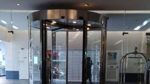 A revolving door with a glass enclosure, a polished wooden floor, and a cart with a logo on it. - The SCENIC: Comfortable living by Awsom Phil (Manila)