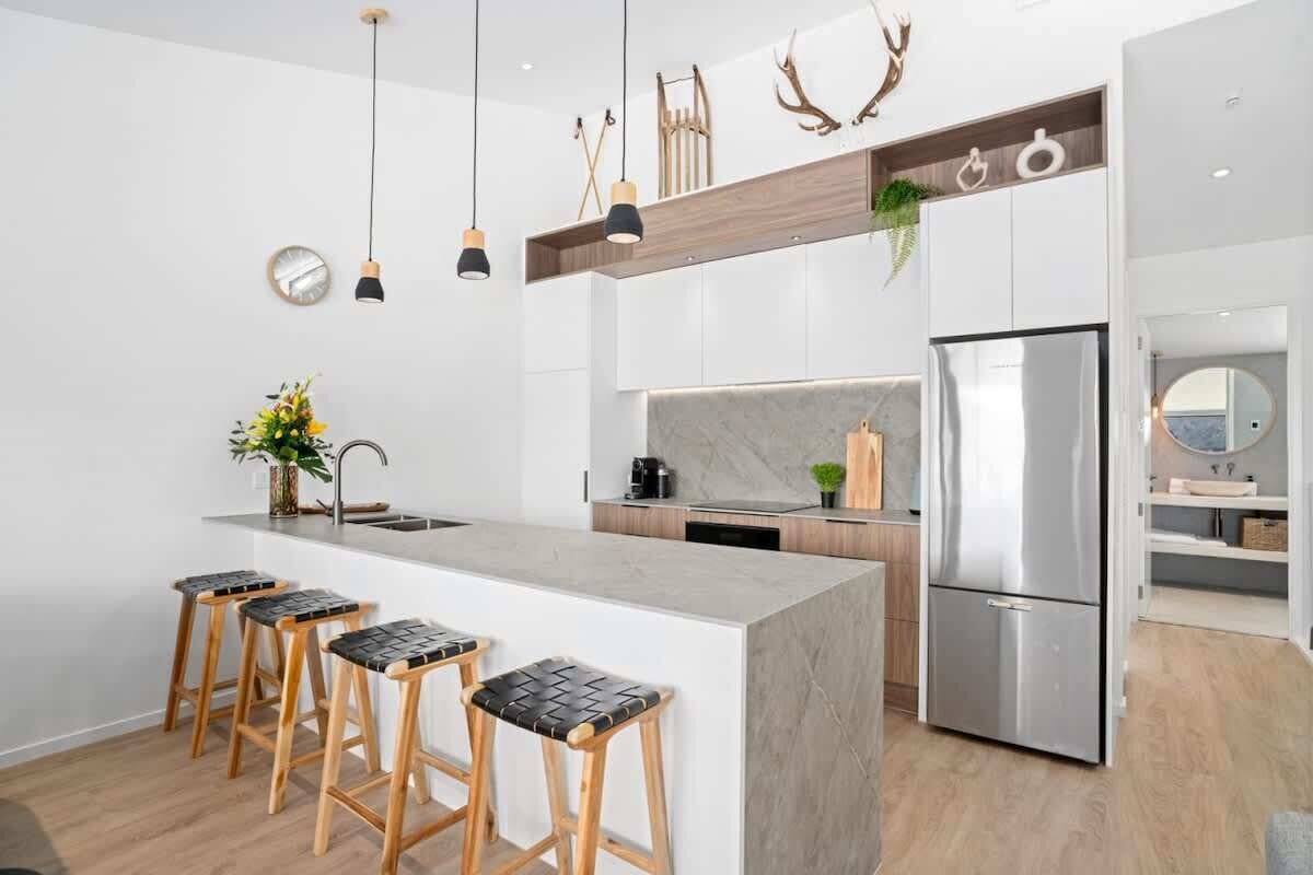 A modern kitchen with a central island, bar stools, a stainless steel refrigerator, and pendant lighting.