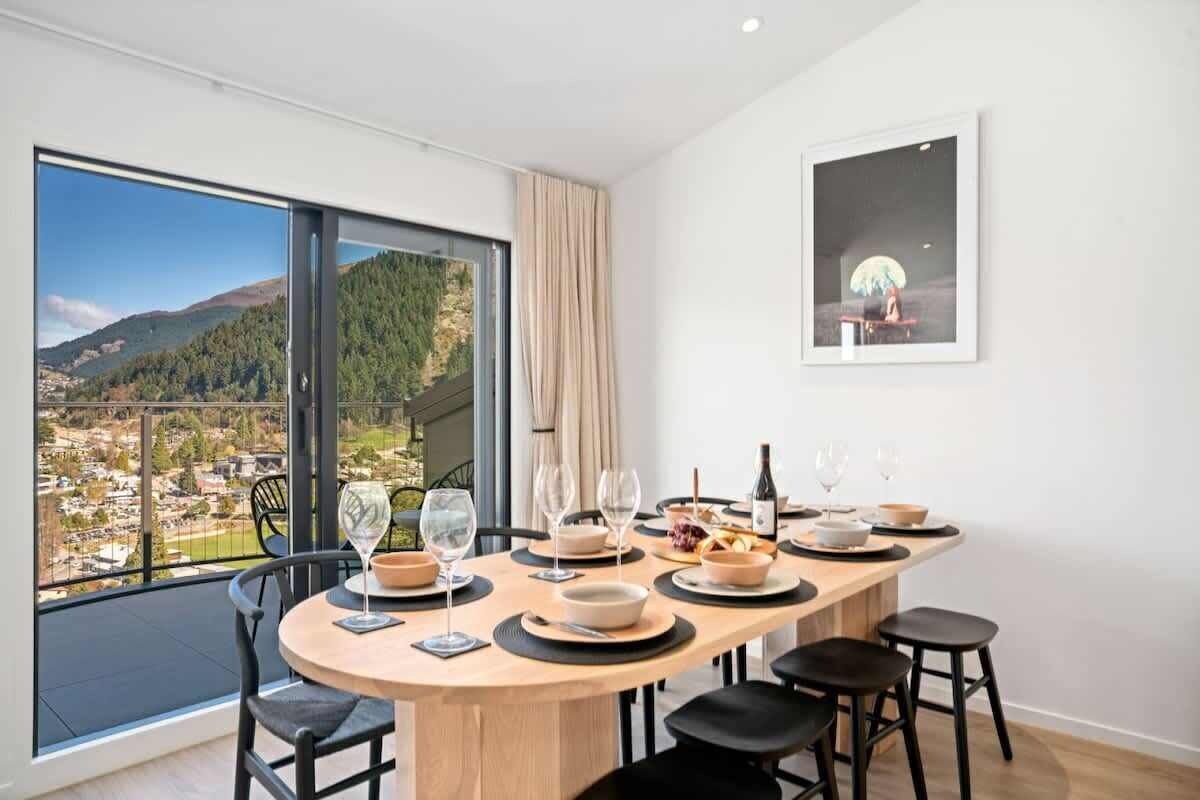 A dining area with a panoramic view of a town and mountains, a table set for four, and a framed picture on the wall.