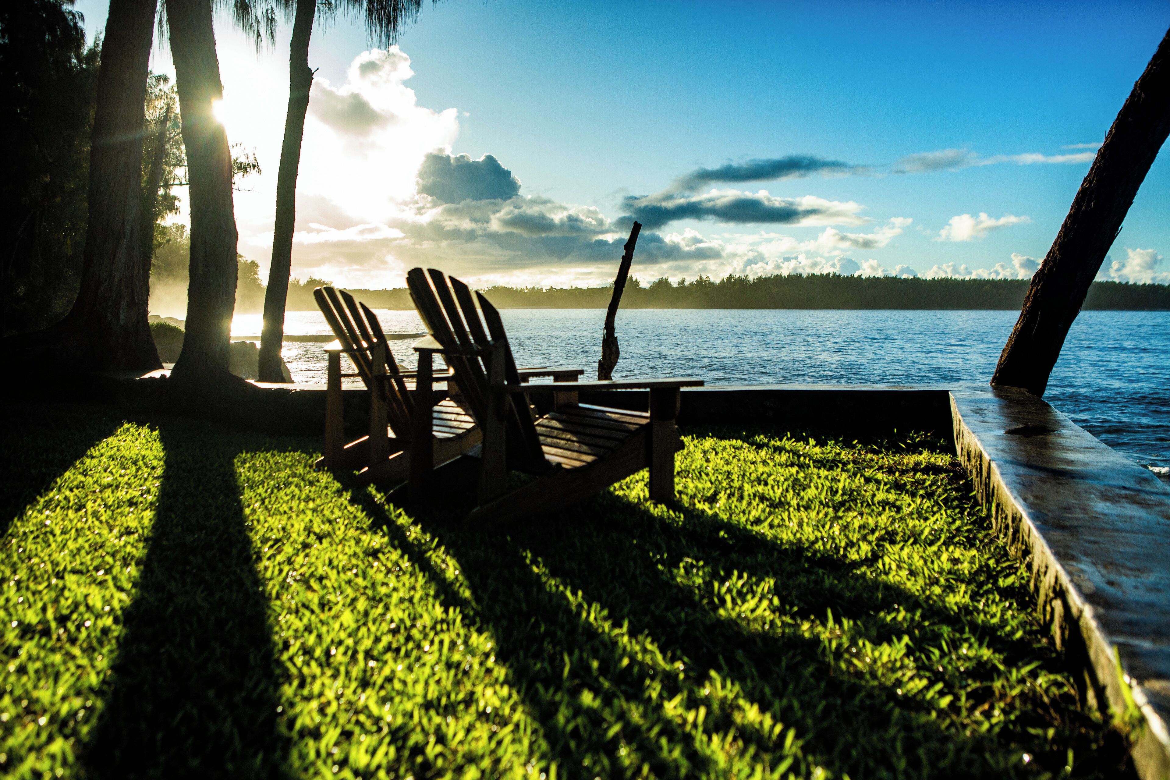Een terras met stoelen met uitzicht op een wateroppervlak, omgeven door gras en bomen.