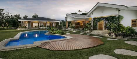 Una casa moderna con piscina, terraza de madera y jardín cuidado.