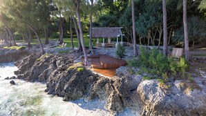 A wooden deck with a thatched-roof structure, surrounded by rocks and greenery. - Nakatumble (Mele)