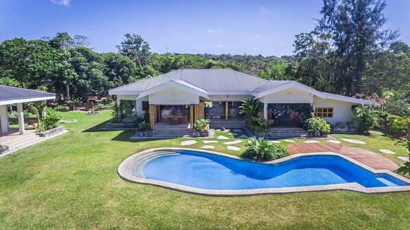 Una casa de dos pisos con piscina, rodeada de un césped cuidado y diversas plantas.