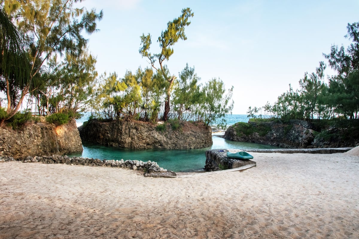 Uma praia com águas turquesa cristalinas, formações rochosas e vegetação exuberante.