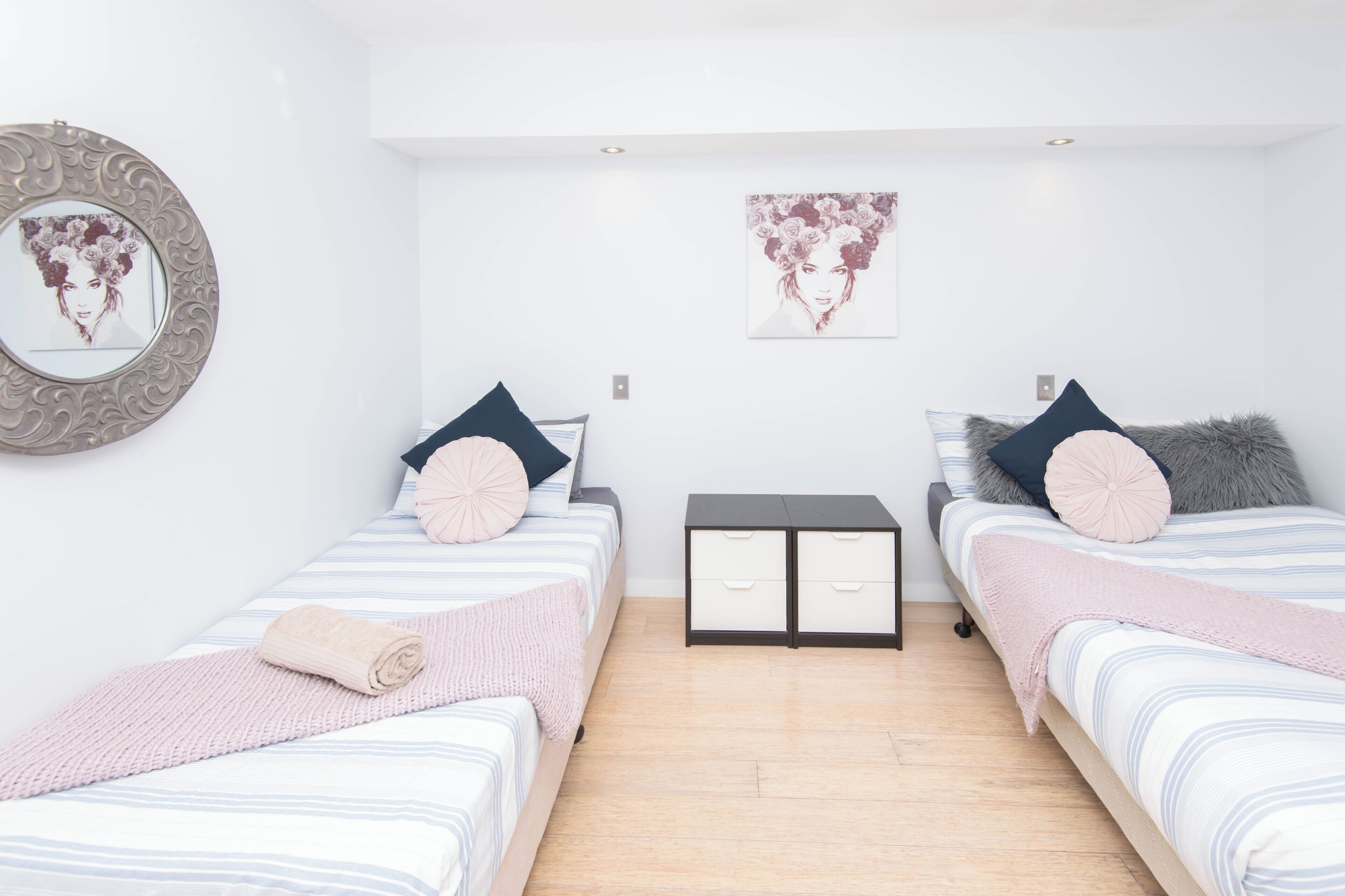 A bedroom with two beds, a nightstand, a dresser, and a mirror.