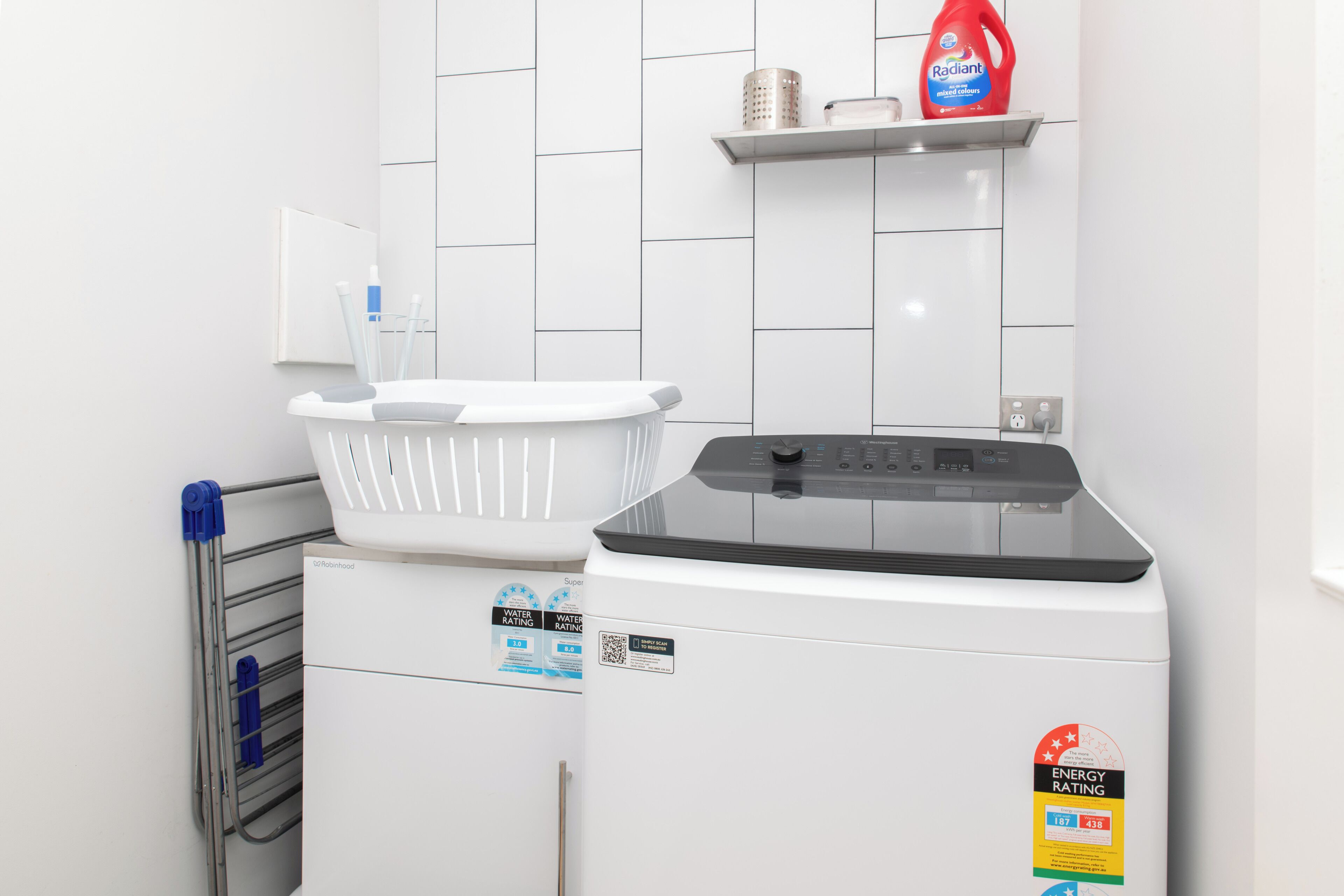 A laundry area with a washing machine, a drying rack, and a shelf with a bottle of detergent.