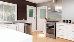 Une cuisine moderne avec des meubles blancs, des appareils en acier inoxydable et une grande fenêtre équipée de stores.