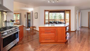 A kitchen with wooden cabinets, a stove, and a dining area with a table and chairs. - Tranquility at Cascade (Norfolk Island)