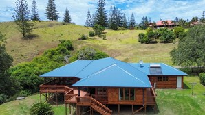 A two-story wooden house with a blue roof, a deck, and a staircase leading to the upper level. - Tranquility at Cascade (Norfolk Island)