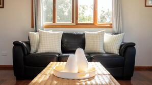 A black leather sofa with checkered pillows, a woven tray table, and two white conical objects on it. - Tranquility at Cascade (Norfolk Island)