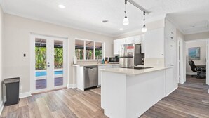 A modern kitchen with a central island, stainless steel appliances, and a view of a swimming pool through glass doors.