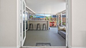 A covered patio area with a bar counter, stools, and a seating area.