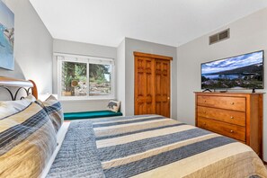 A bedroom with a bed, a wooden dresser, a television, a window with a view of greenery, and a door. - Walk to Lake Tahoe - Pet-Friendly Cabin - Sleeps 7, Kids Welcome (Carnelian Bay)