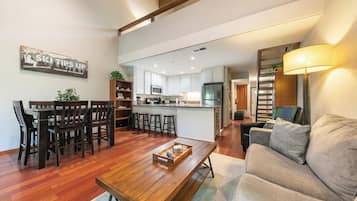 A spacious living area with a wooden coffee table, a sofa, and a dining table with chairs.