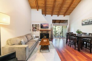 A living room with a sofa, coffee table, fireplace, dining table with chairs, and a balcony with a view. - Walk to Lake Tahoe - Pet-Friendly Cabin - Sleeps 7, Kids Welcome (Carnelian Bay)