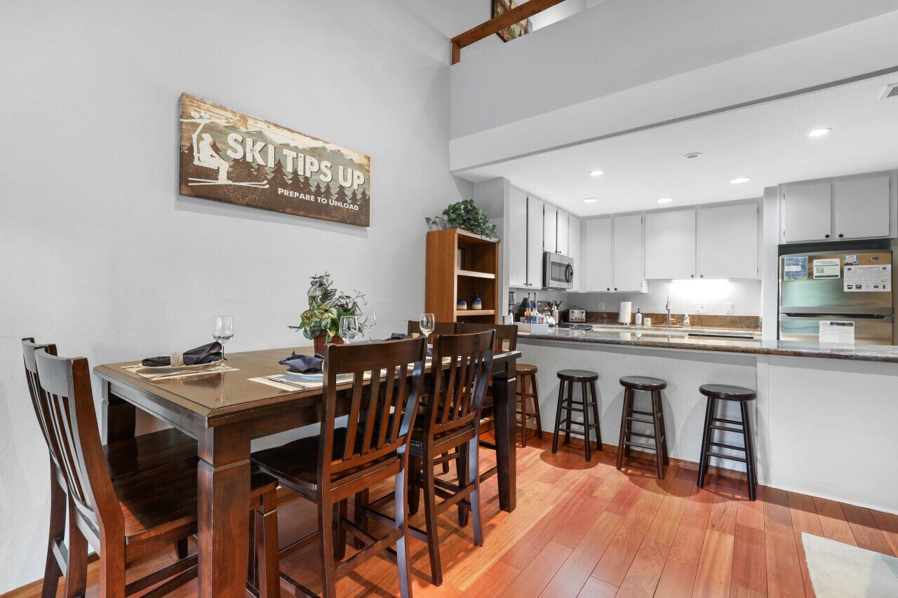 A modern kitchen with a wooden dining table, bar stools, and a kitchen island.