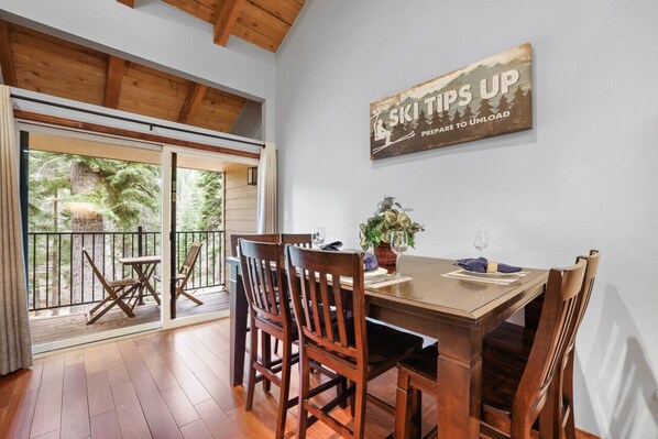 A dining area with a wooden table, chairs, and a view through large sliding glass doors to a balcony. - Walk to Lake Tahoe - Pet-Friendly Cabin - Sleeps 7, Kids Welcome (Carnelian Bay)