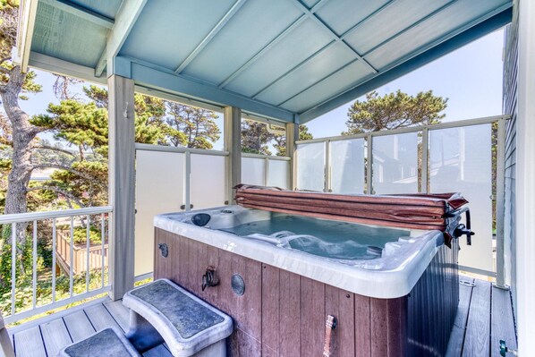 A hot tub on a wooden deck with a glass enclosure, surrounded by trees.