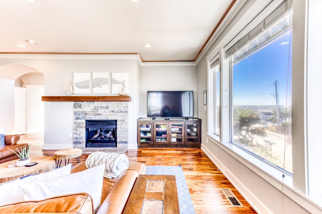 A spacious living room with a fireplace, a television, and a large window offering a view of the outdoors.