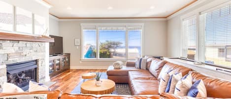 A living room with a stone fireplace, leather sofa, and large windows.
