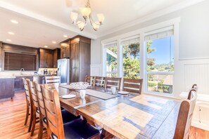 Un comedor amplio con una gran mesa de madera y sillas, una cocina con armarios oscuros y ventanas amplias que ofrecen vistas al exterior.