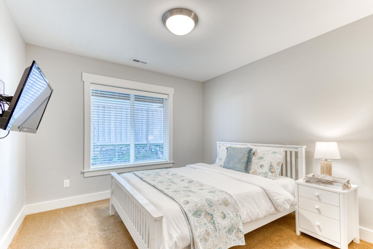 Une chambre à coucher comprenant un lit, une table de chevet, une lampe, une fenêtre avec des stores et un luminaire au plafond.