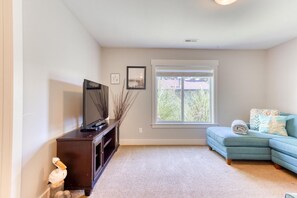 A living room with a television on a wooden stand, a blue sofa, a window with blinds, and a carpeted floor.