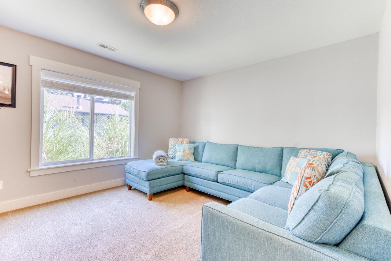 A living room with a sectional sofa, a small ottoman, and a large window providing a view of greenery outside.