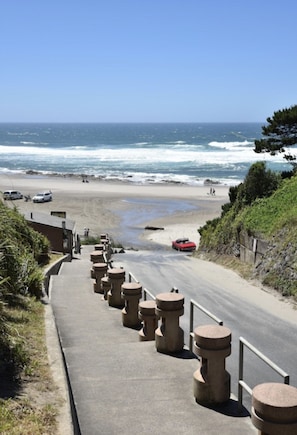 Una carretera costera con vista a la playa, pilares de hormigón y un coche rojo.
