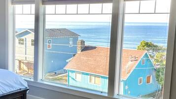 A bedroom with a large window overlooking a beach and houses.